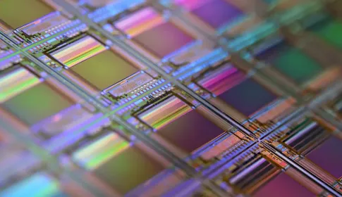 A silicon wafer photographed close up, its repeating processor dies refracting rainbow colours.