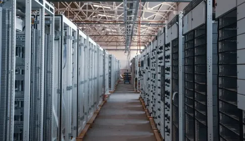 A walkway running between tall grey storage racks in a brightly lit data center hall.