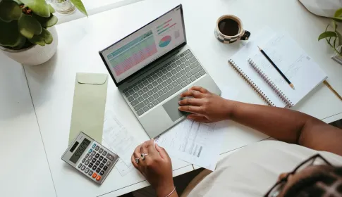 An overhead view of a desk with a laptop showing a budget spreadsheet, a calculator, and a notebook.