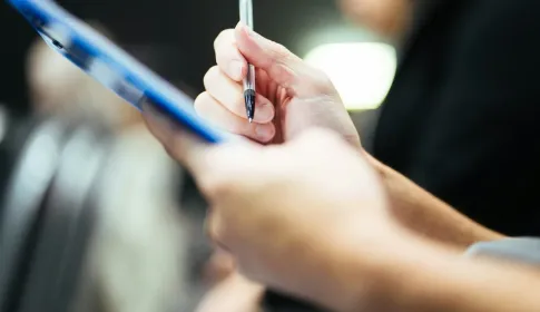 A hand holding a pen over a clipboard while taking notes during an assessment.