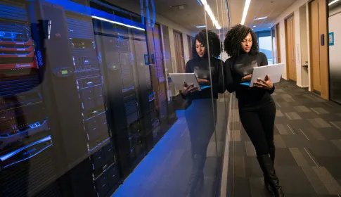 A technology professional holding a laptop beside racks of data center equipment.