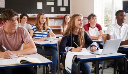 Diverse middle school students attentively listening and taking notes at their desks in a bright classroom.