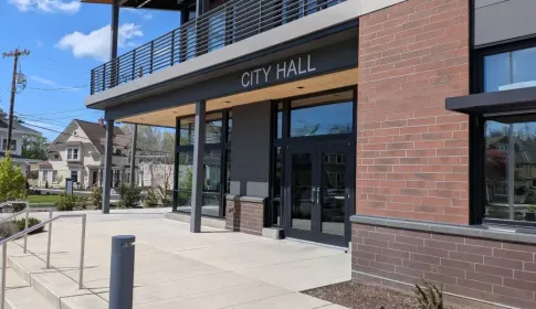 Modern city hall entrance with a brick facade, glass doors, an accessible ramp and a second-floor balcony.