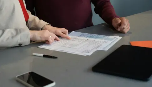 Two people seated at a desk reviewing printed statements and documents together.