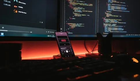 A workstation at night with source code on two monitors and a phone on a stand.