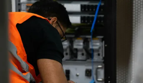 A technician in a high visibility vest working on equipment inside an open server rack.