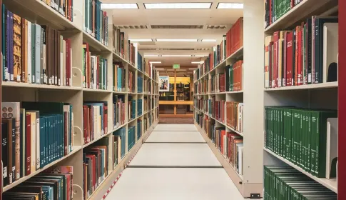 A corridor running between tall library shelves filled with bound volumes.