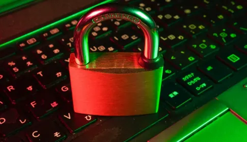 A metal padlock closed on top of an illuminated computer keyboard.