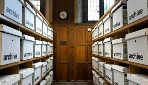 Rows of white storage boxes marked archive, shelved on either side of a wooden door.