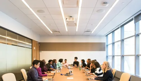 People meeting around a long boardroom table with laptops and papers.