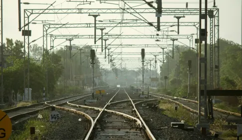 Railway tracks converging beneath overhead lines and signal gantries.