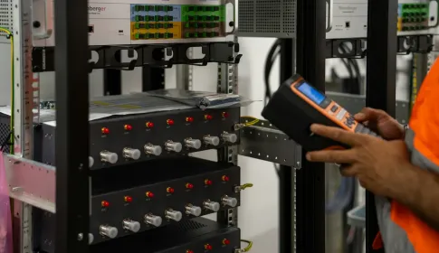 A technician inspecting network equipment racks with a handheld diagnostic tool.