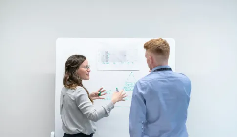 Two colleagues at a whiteboard working through a process framework diagram.