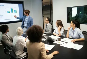Business professional presents 2018 budget cash flow charts to a diverse team of six colleagues in a modern conference room.
