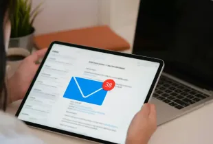 Professional reviewing an email inbox with 38 unread messages on a tablet; with a laptop in the background.