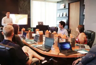 IT professionals attending a boardroom presentation with laptops and gift bags on a conference table.