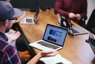 IT professionals collaborate around a wooden table with several laptops open during a team strategy meeting.