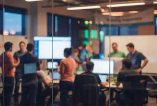 IT professionals collaborating in a modern office, working at computers and whiteboards during a team strategy session.