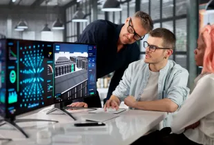 IT professionals collaborate at a workstation reviewing 3D data center and network analytics dashboards on dual monitors.