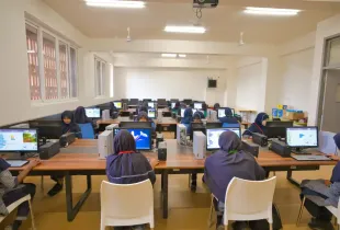 Female students in hijabs working on desktop computers in a school computer lab; using Scratch programming software.