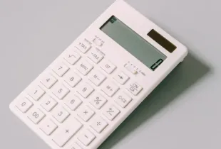 A plain white desk calculator lying on a light grey surface.