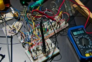 A breadboard prototype crowded with tangled coloured jumper wires, with a multimeter beside it.