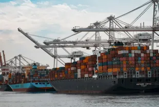 A container ship stacked with freight containers alongside gantry cranes at a port.