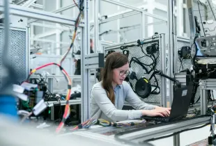 An engineer at a laptop beside an automated production line, monitoring the machinery.