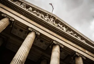 The stone columns and carved pediment of a classical civic building seen from below.