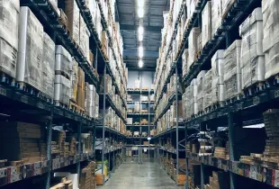 A long aisle between tall warehouse racks stacked with boxed and palletised stock.