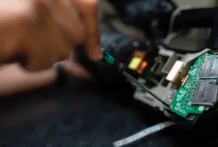 Hands using a small precision tool to examine the exposed circuit boards inside a device.