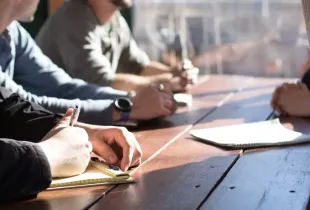 Four colleagues seated along a wooden table, writing notes during a working session.
