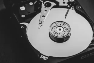 An opened hard disk drive in black and white, showing the platter and the read head arm.