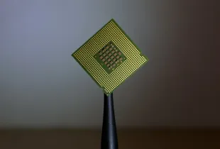 A small gold and green processor die balanced on a black stand against a plain background.