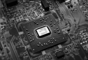 A black and white close view of a processor package mounted on a densely populated circuit board.