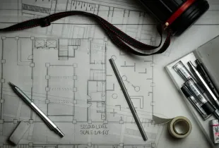 Rolled architectural floor plans on a desk beside a pen, a scale rule and drafting tools.