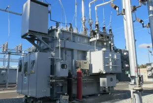 Transformer and switchgear equipment in an electrical substation under a clear blue sky.