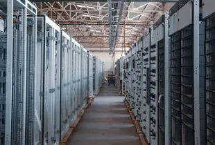 A walkway running between tall grey storage racks in a brightly lit data center hall.