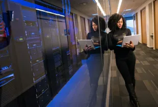 A technology professional holding a laptop beside racks of data center equipment.