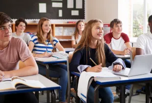 Diverse middle school students attentively listening and taking notes at their desks in a bright classroom.