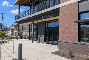 Modern city hall entrance with a brick facade, glass doors, an accessible ramp and a second-floor balcony.