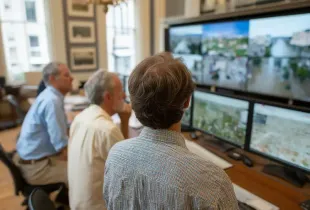 Local government officials monitor flood imagery and mapping data on large display screens in an operations room.