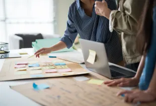 Team members review a large process map covered in colorful sticky notes on a conference table beside a laptop.