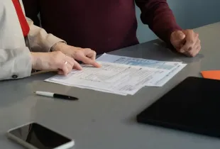 Two people seated at a desk reviewing printed statements and documents together.