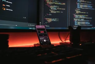 A workstation at night with source code on two monitors and a phone on a stand.