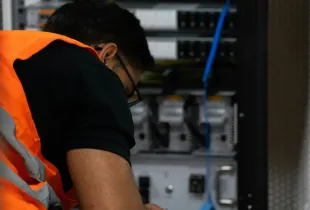 A technician in a high visibility vest working on equipment inside an open server rack.