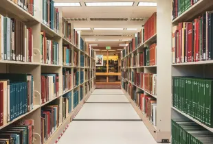 A corridor running between tall library shelves filled with bound volumes.