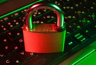 A metal padlock closed on top of an illuminated computer keyboard.