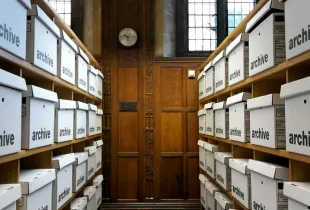 Rows of white storage boxes marked archive, shelved on either side of a wooden door.