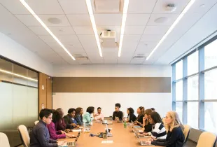 People meeting around a long boardroom table with laptops and papers.